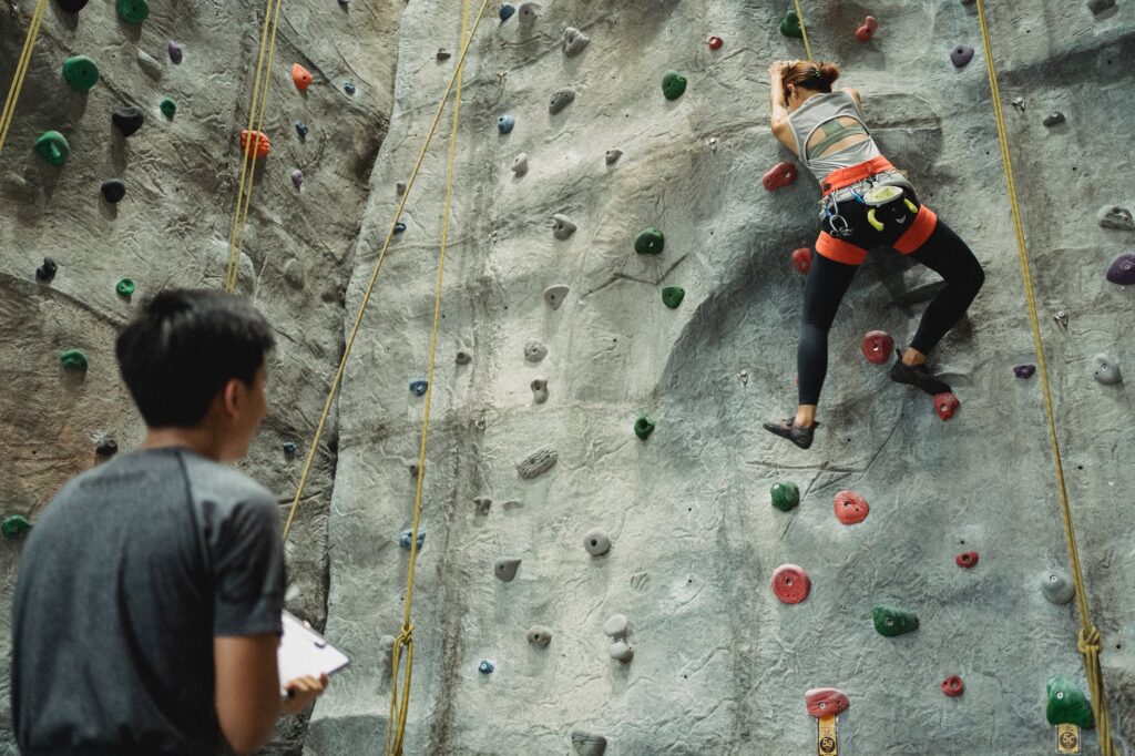 young coach controlling climber training on rocky wall